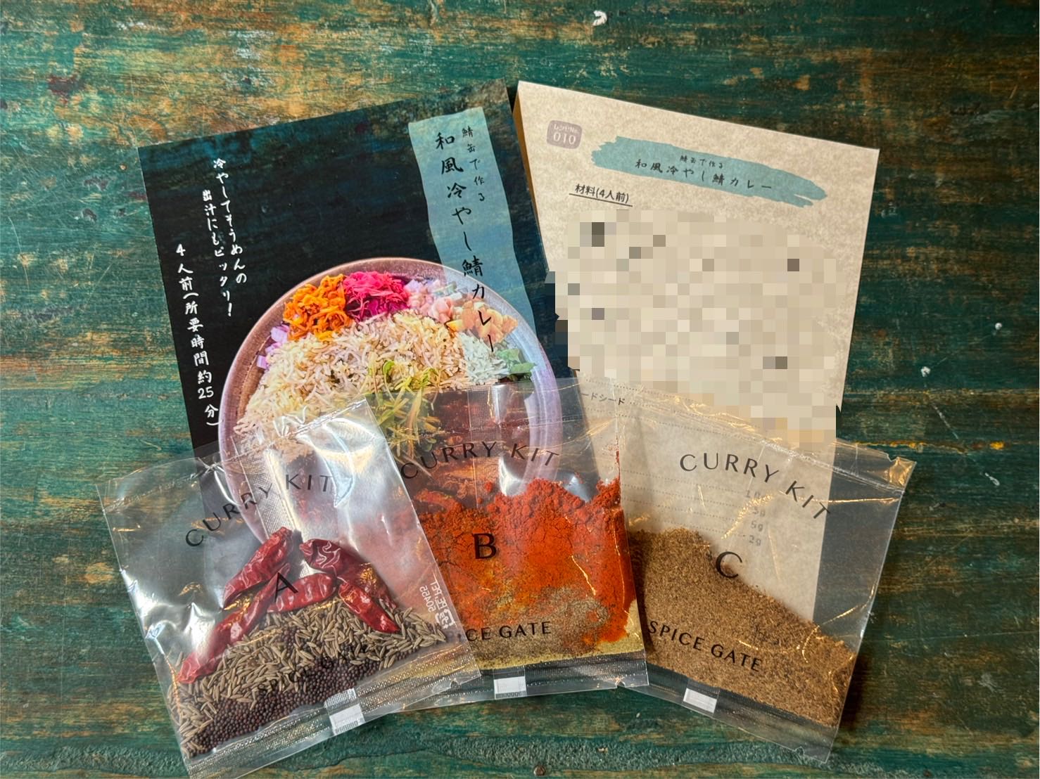 『和風冷やし鯖カレー』キットの中身。スパイス3袋（A・B・C）と店頭の紹介カード、レシピ用紙が並んでいる